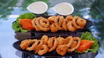 A plate of fried calamari rings with lemon wedges and lettuce, accompanied by two small bowls of dipping sauce.