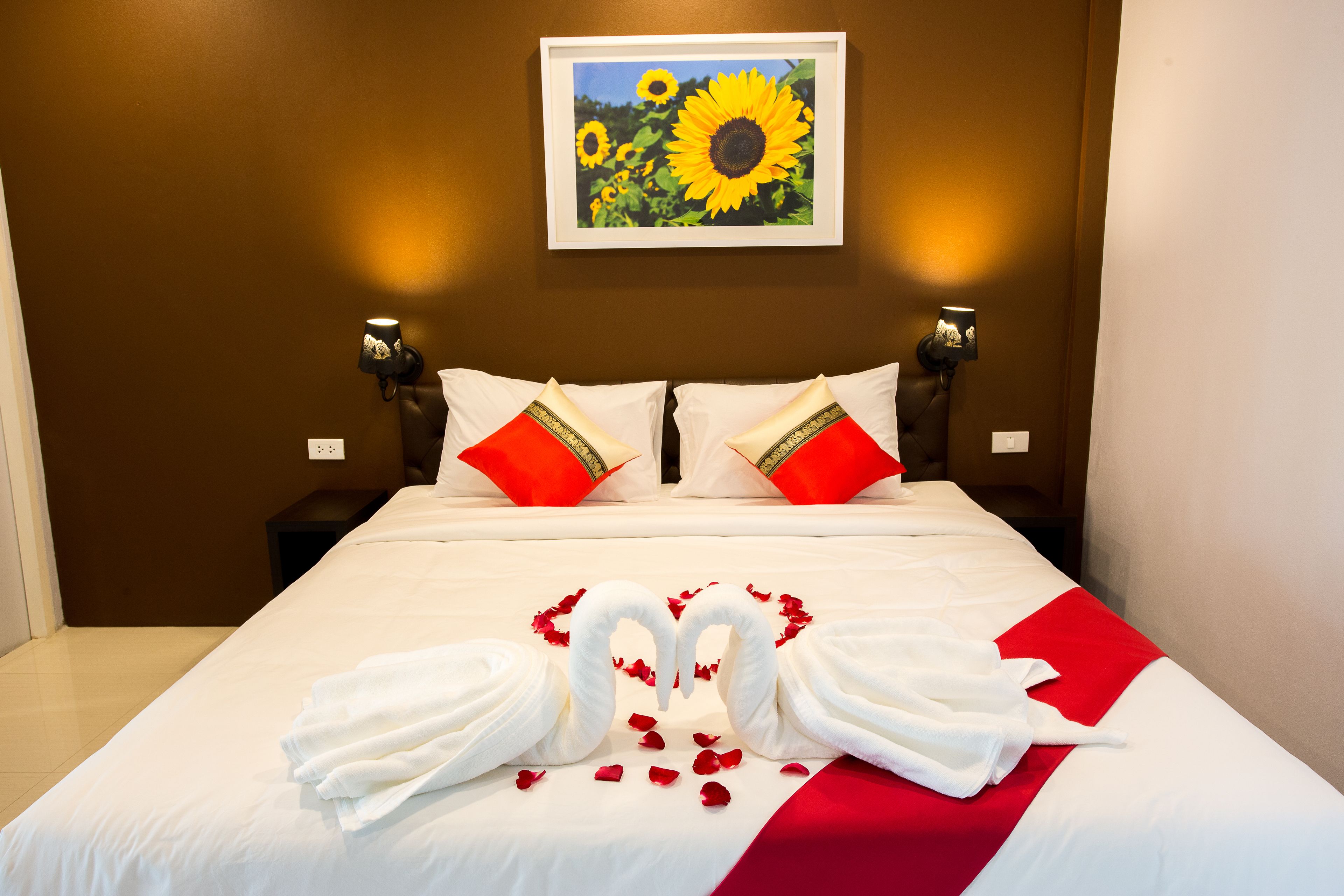 Una cama bien hecha con sábanas blancas, almohadas rojas y un corredor de cama a rayas rojas y blancas. Hay dos lámparas de pared a cada lado de la cama.