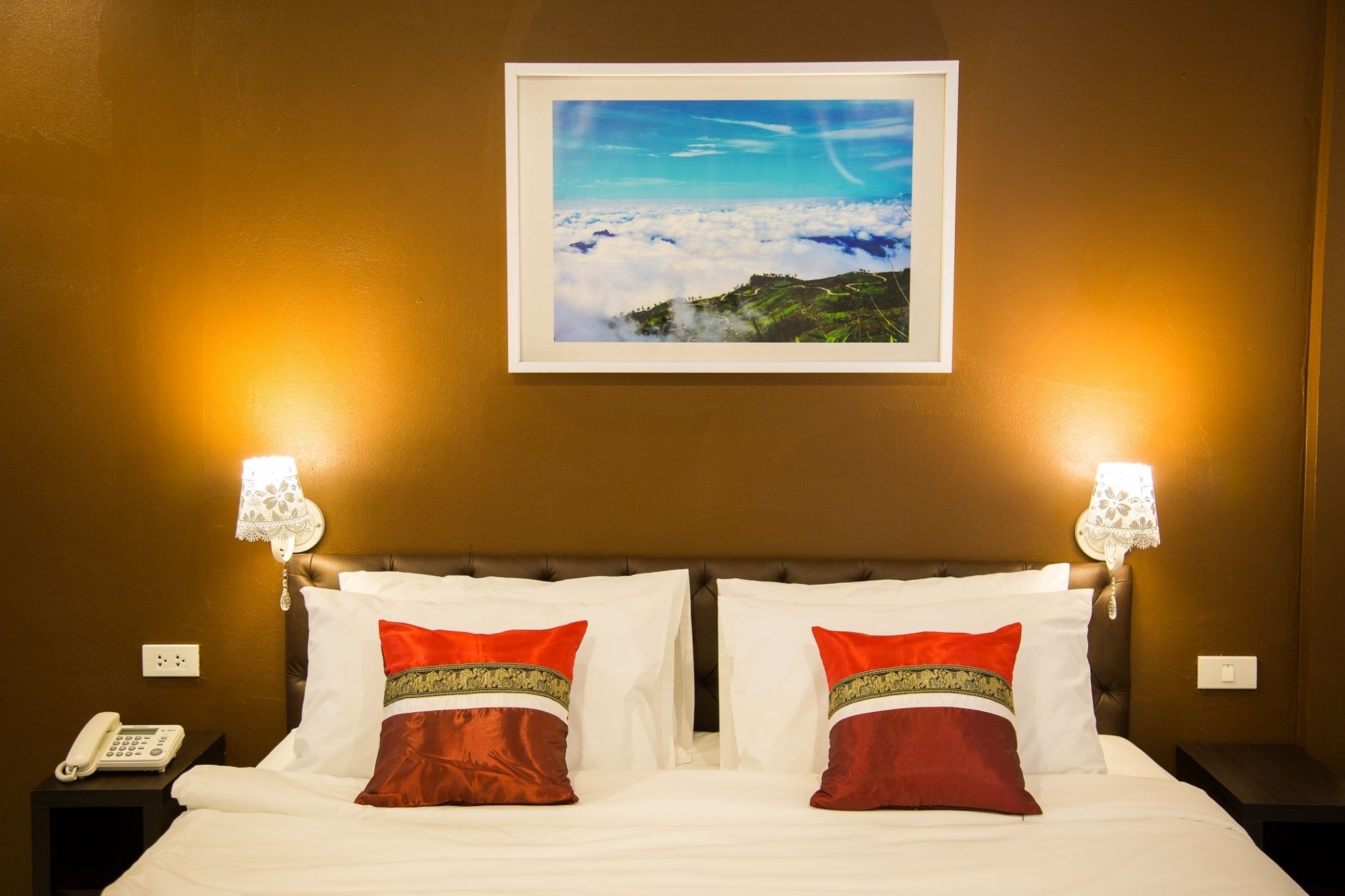 A hotel room with a bed, two bedside lamps, a framed picture on the wall, and a telephone on the nightstand.
