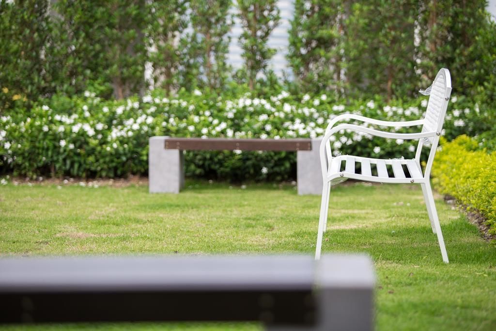 A white metal chair and a bench in a grassy area with a backdrop of trees and white flowers.