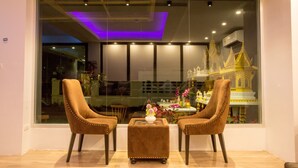 Una habitación moderna con dos sillones tapizados en marrón, un pequeño taburete cuadrado y un ventanal con vistas a un templo dorado.