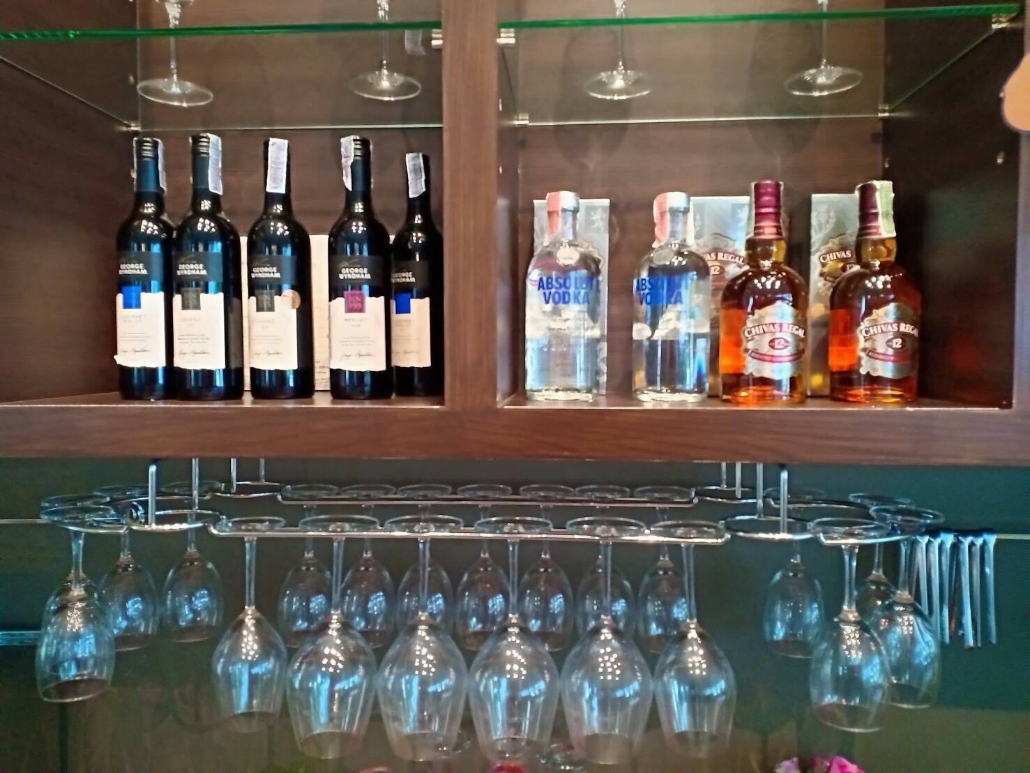 A bar area with multiple bottles of vodka and whiskey, and several empty wine glasses hanging below.