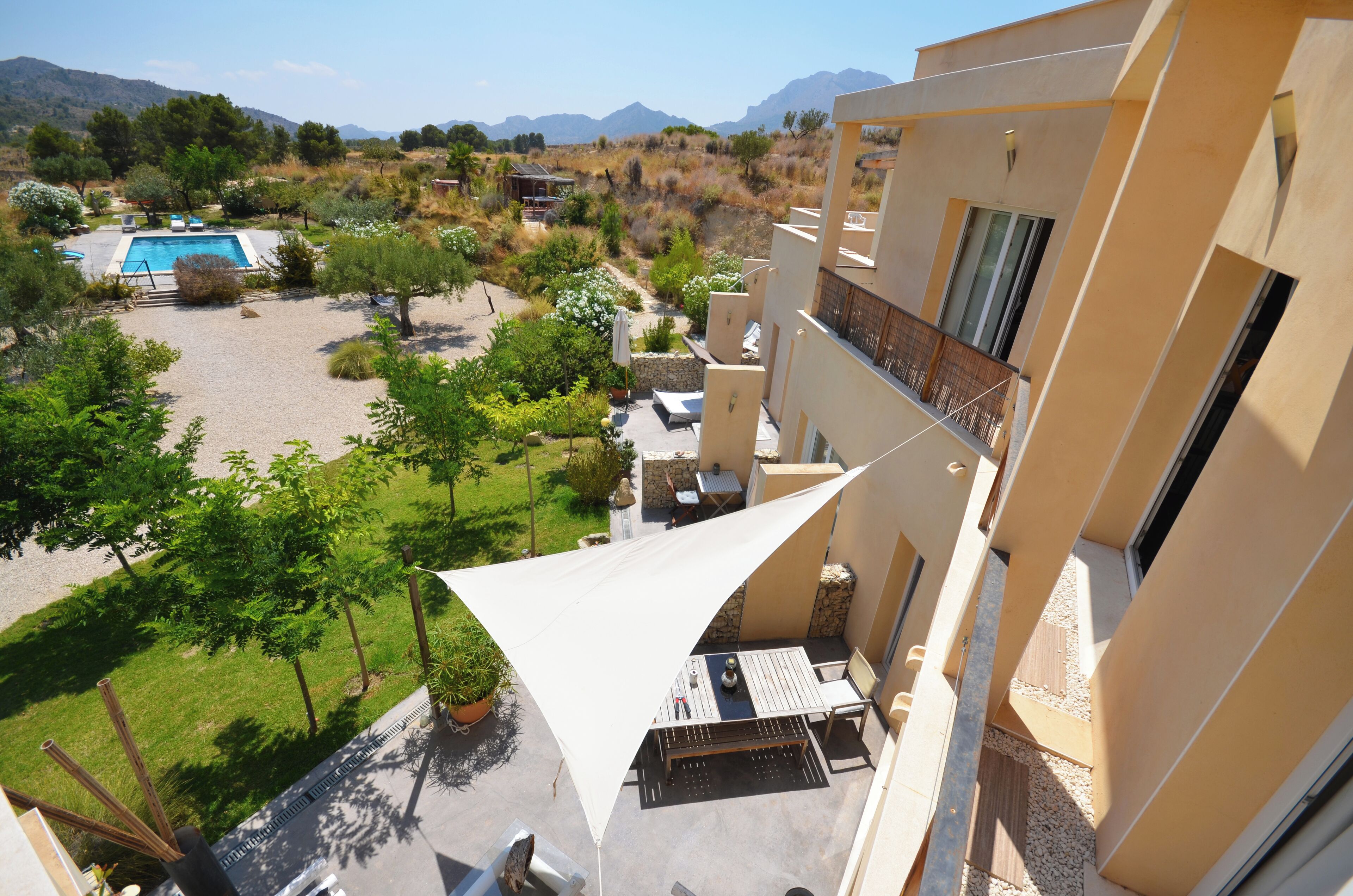 Un área de piscina con vistas a montañas, un patio con mobiliario exterior y un edificio con balcones.