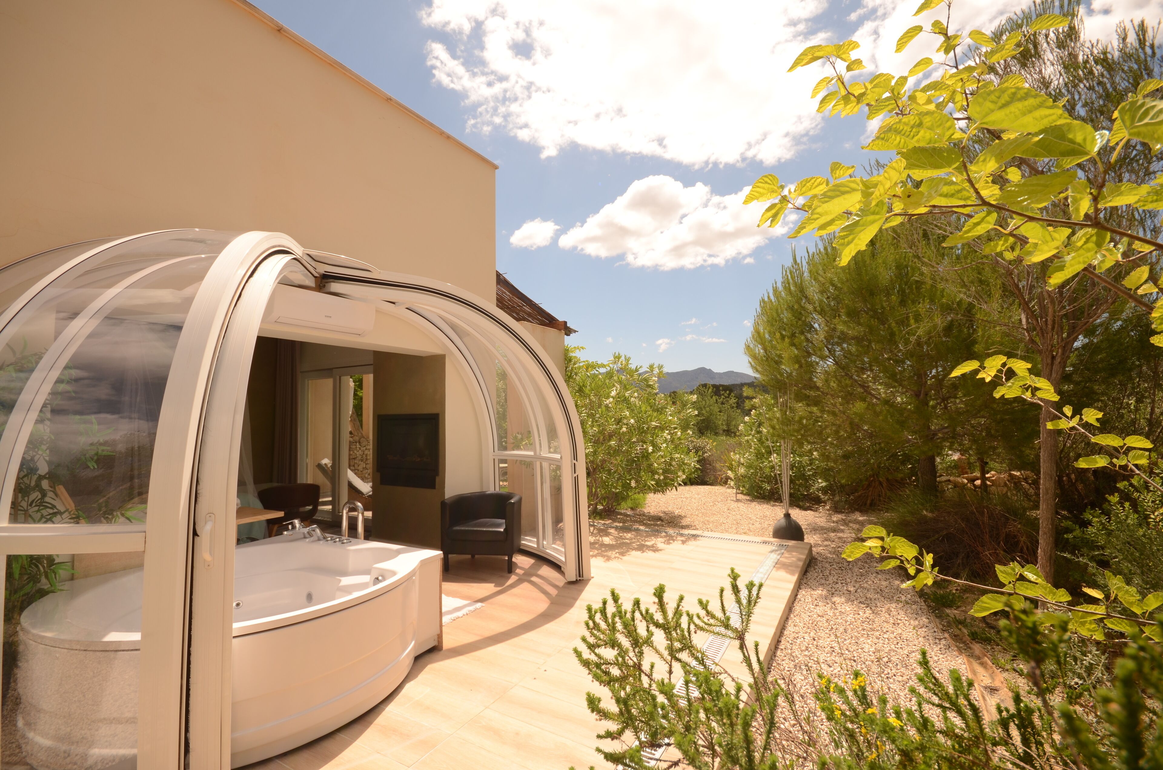 A modern spa with a glass-enclosed hot tub, a seating area, and a view of a landscaped garden.