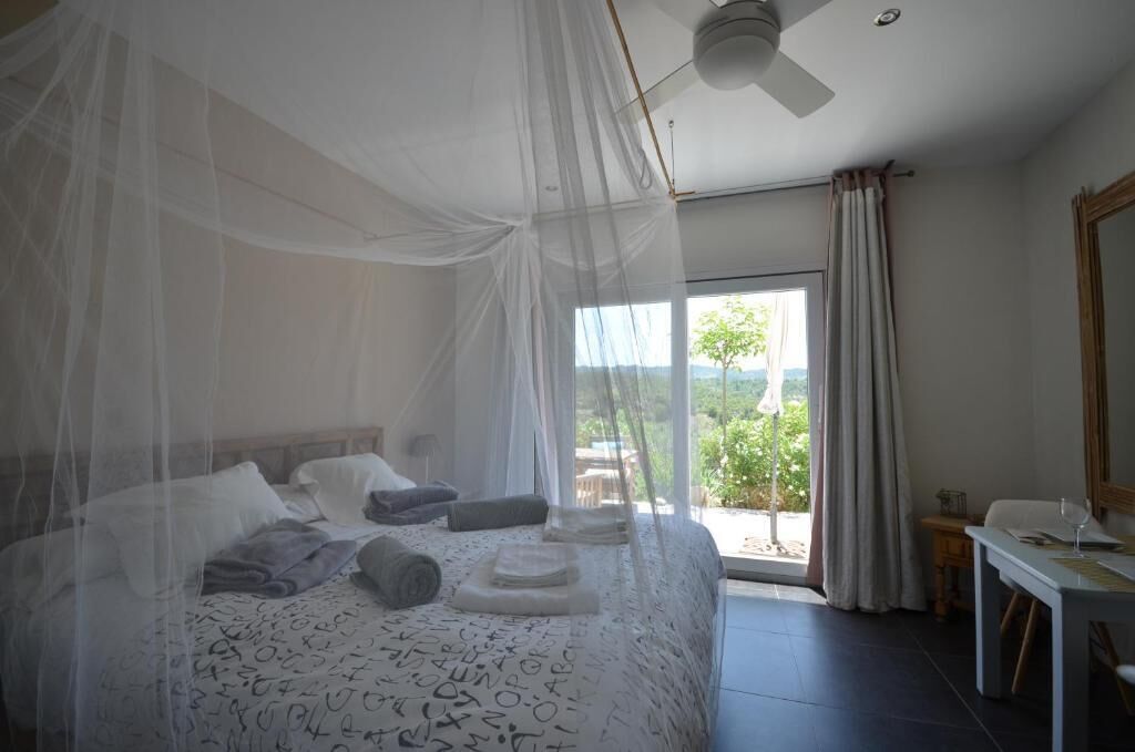 A bedroom with a bed covered by a canopy, a desk, and a view of the outdoors.