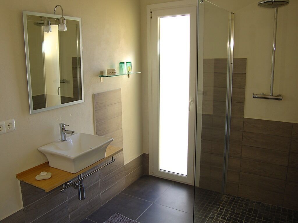 A modern bathroom with a white sink, a glass shower enclosure, and a large mirror.