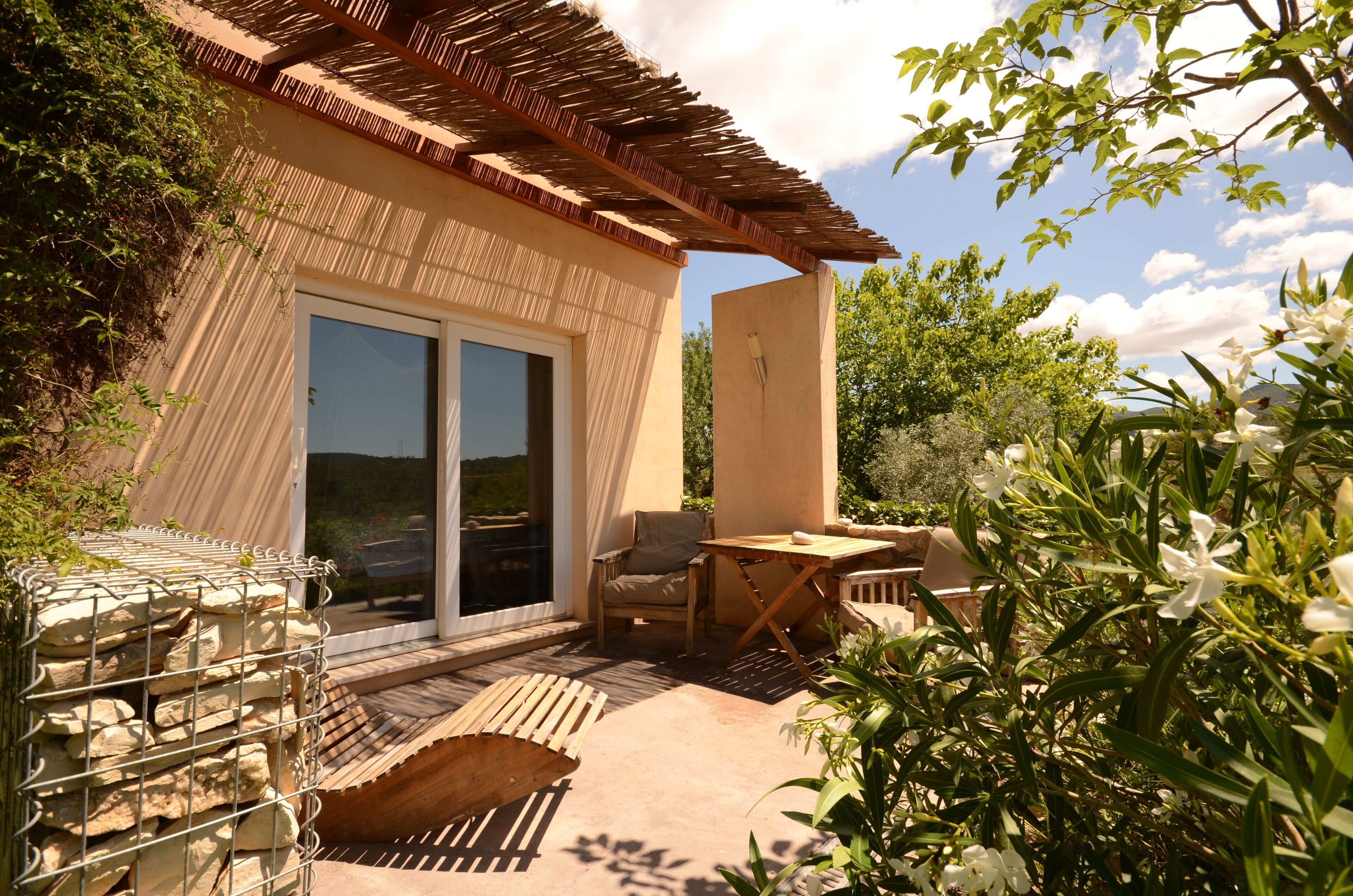A patio with a wooden table and chairs, a stone wall, and a view of the surrounding greenery.