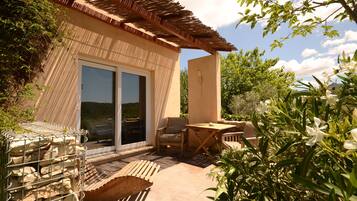 A patio with a wooden table and chairs, a stone wall, and a view of the surrounding greenery.