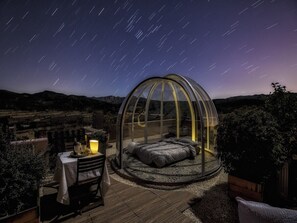 Una habitación abovedada con una cama, una mesa con una vela y vistas al cielo nocturno.