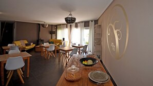 A modern dining area with wooden tables and chairs, a yellow sofa, and a decorative wall with a logo. - El Pao  (Jijona)
