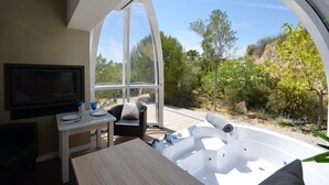 A modern room with a large window, a TV, a table, a chair, and a hot tub. - El Pao  (Jijona)
