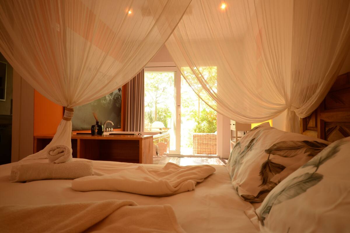 A bedroom with a canopy bed, a desk, and a view of the outdoors.