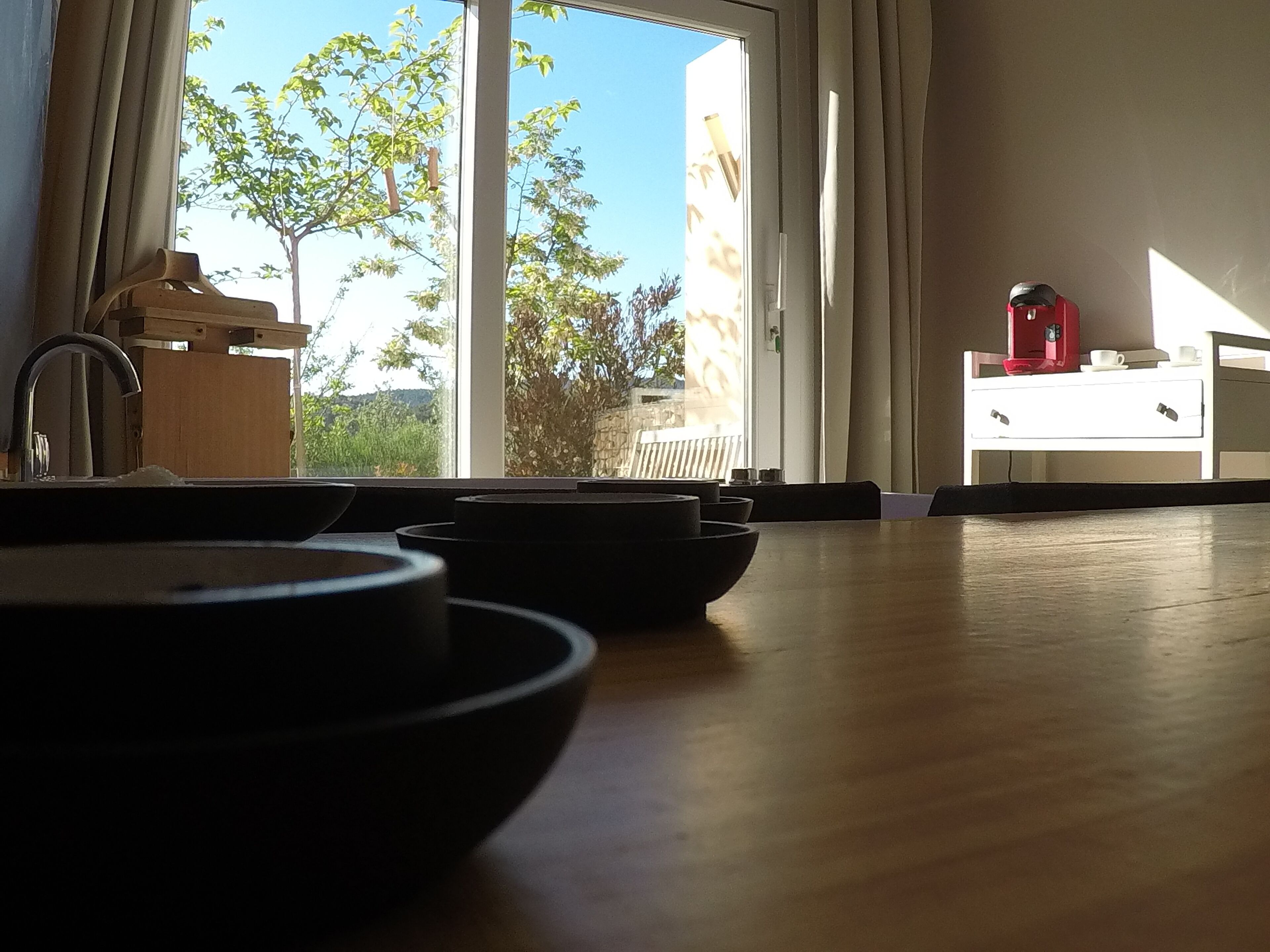 Ein Zimmer mit Holztisch, Kaffeemaschine und Blick auf Bäume und ein Gebäude.