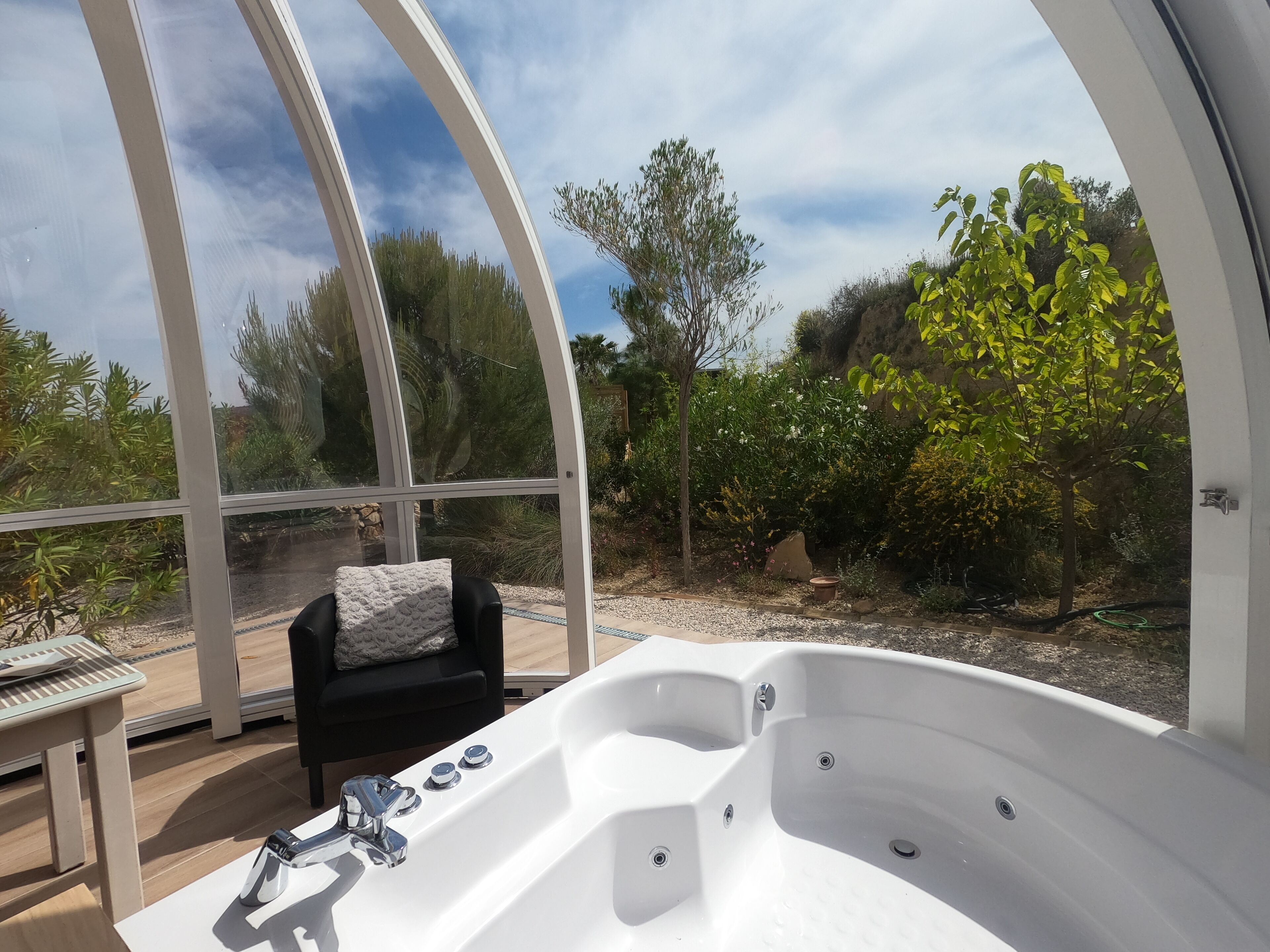 A hot tub in a glass-enclosed room with a view of a garden and trees.
