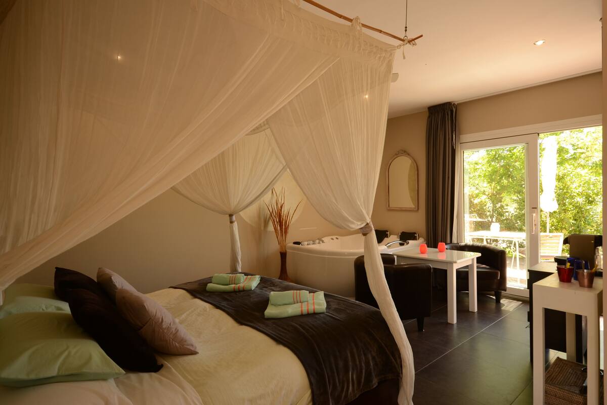 A bedroom with a canopy bed, a sitting area with a table and chairs, and a view of the outdoors.