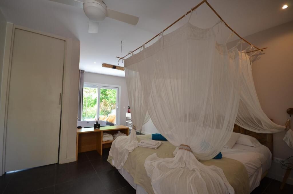 A bedroom with a canopy bed, a desk with a chair, and a window with a view of greenery.