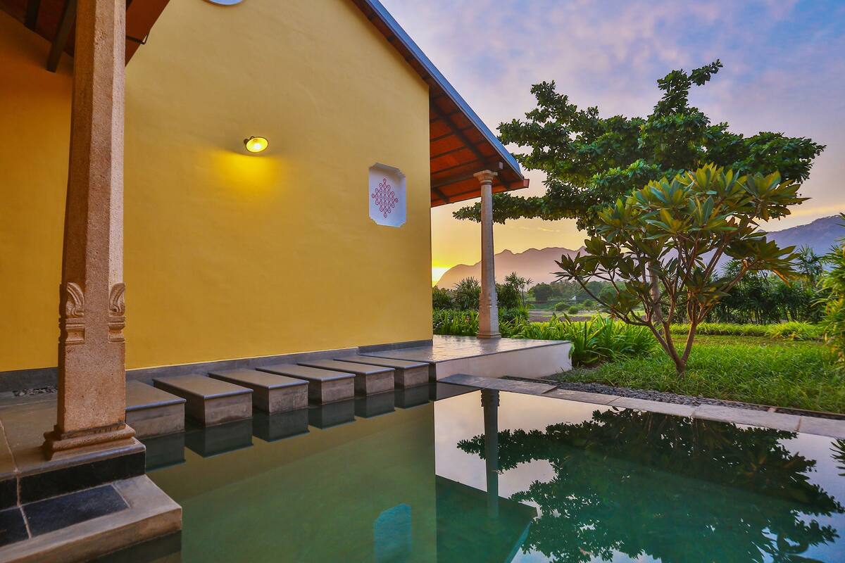 Zona de piscina con un borde de piedra y un edificio con pared amarilla y techo de madera.