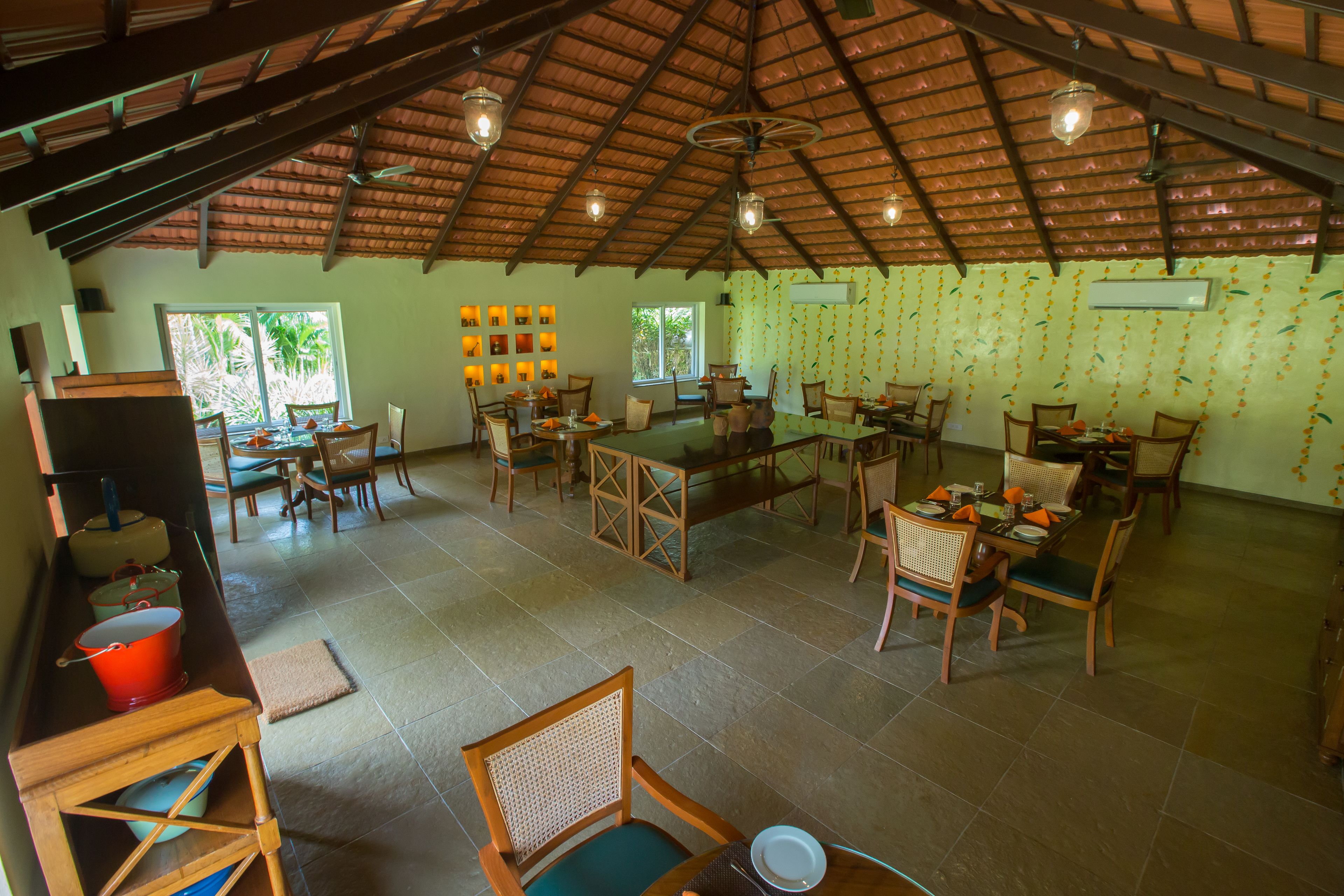 A spacious dining area with multiple tables and chairs, a high ceiling with exposed beams, and large windows providing natural light.