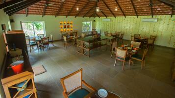A spacious dining area with multiple tables and chairs, a high ceiling with exposed beams, and large windows providing natural light.