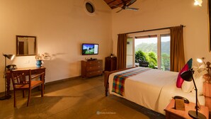 A hotel room with a bed, desk, chair, TV, and a window with curtains. - Dvara Siruvani (Coimbatore)