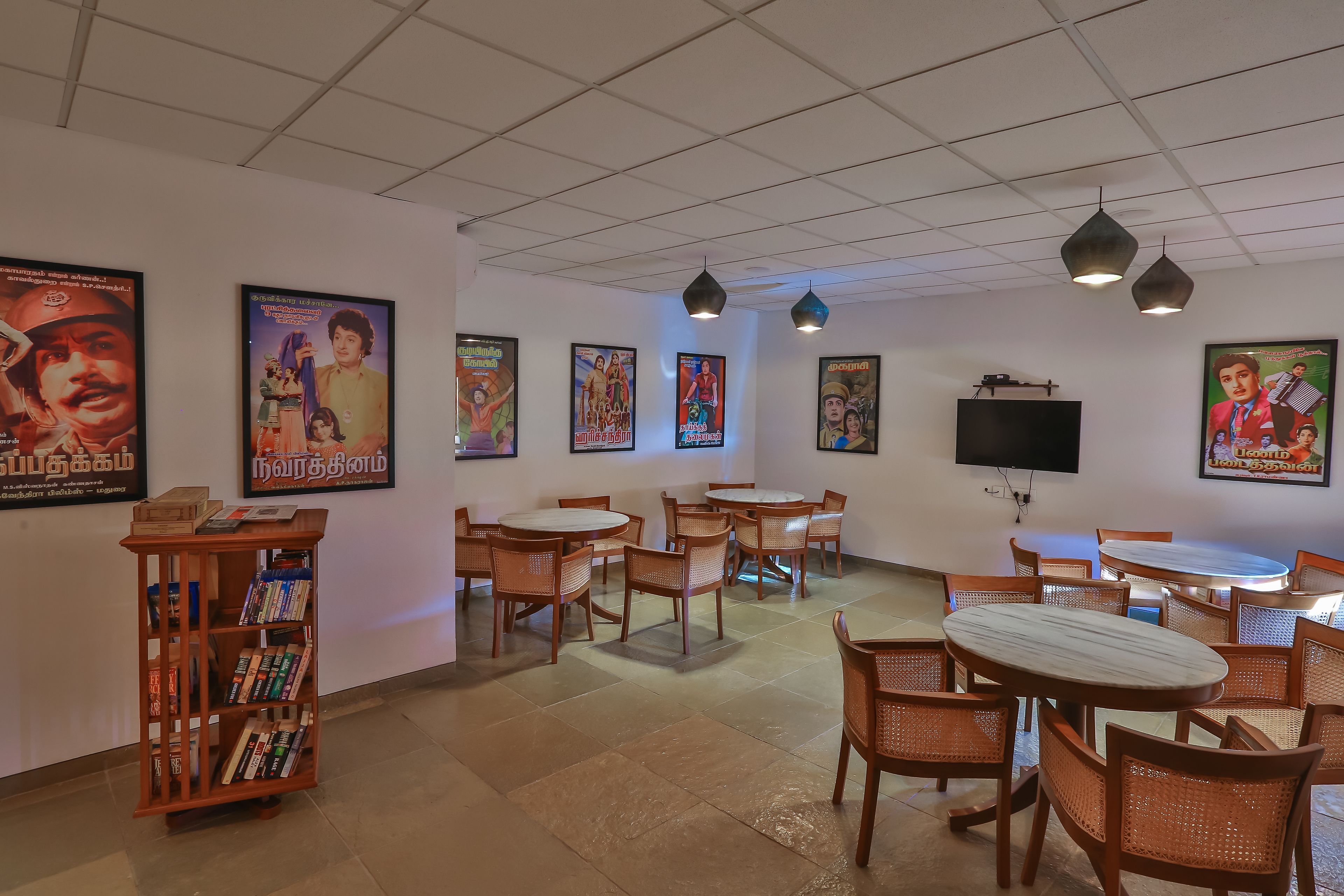 A restaurant with multiple tables and chairs, posters on the walls, and a bookshelf with books.