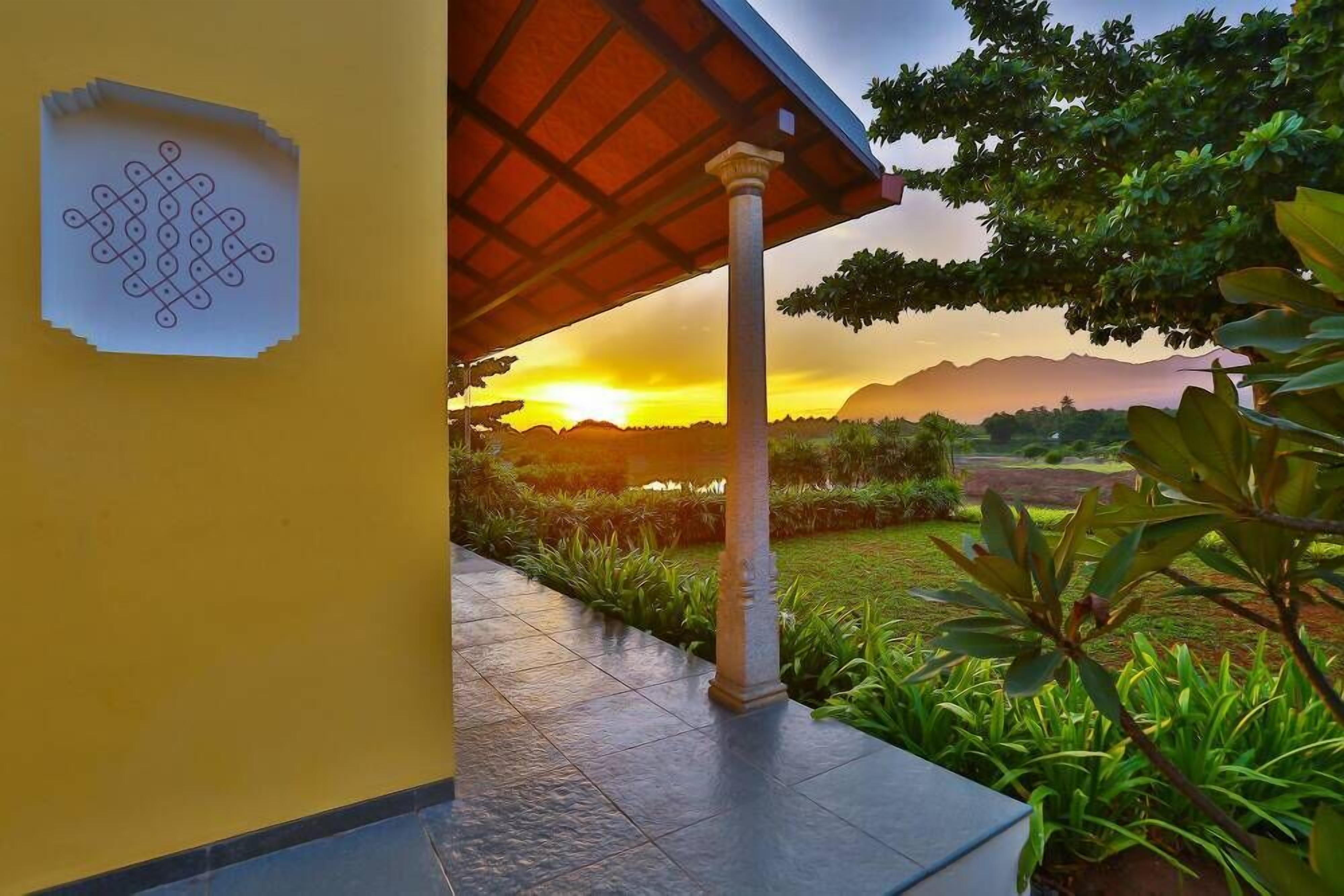 A covered outdoor area with a tiled floor, a column, and a view of a sunset over a landscape with mountains.