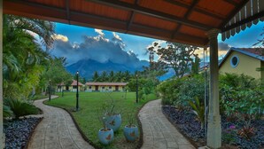 A paved pathway leading to a building with a covered entrance, surrounded by lush greenery and a mountainous backdrop. - Dvara Siruvani (Coimbatore)