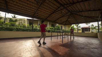 An open covered area with a concrete floor, a metal table, and a person in a red shirt and shorts.