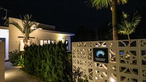 Moderne resort ingang met een bordje voor United Resort Kibougoka, omgeven door groen en palmbomen.