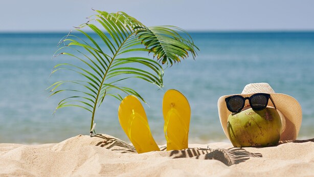 Een strandscène met een palmboom, gele slippers, een kokosnoot en een strohoed.