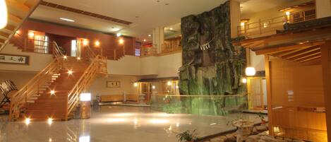 A spacious lobby with a central staircase, a rock wall feature, and a small garden area.