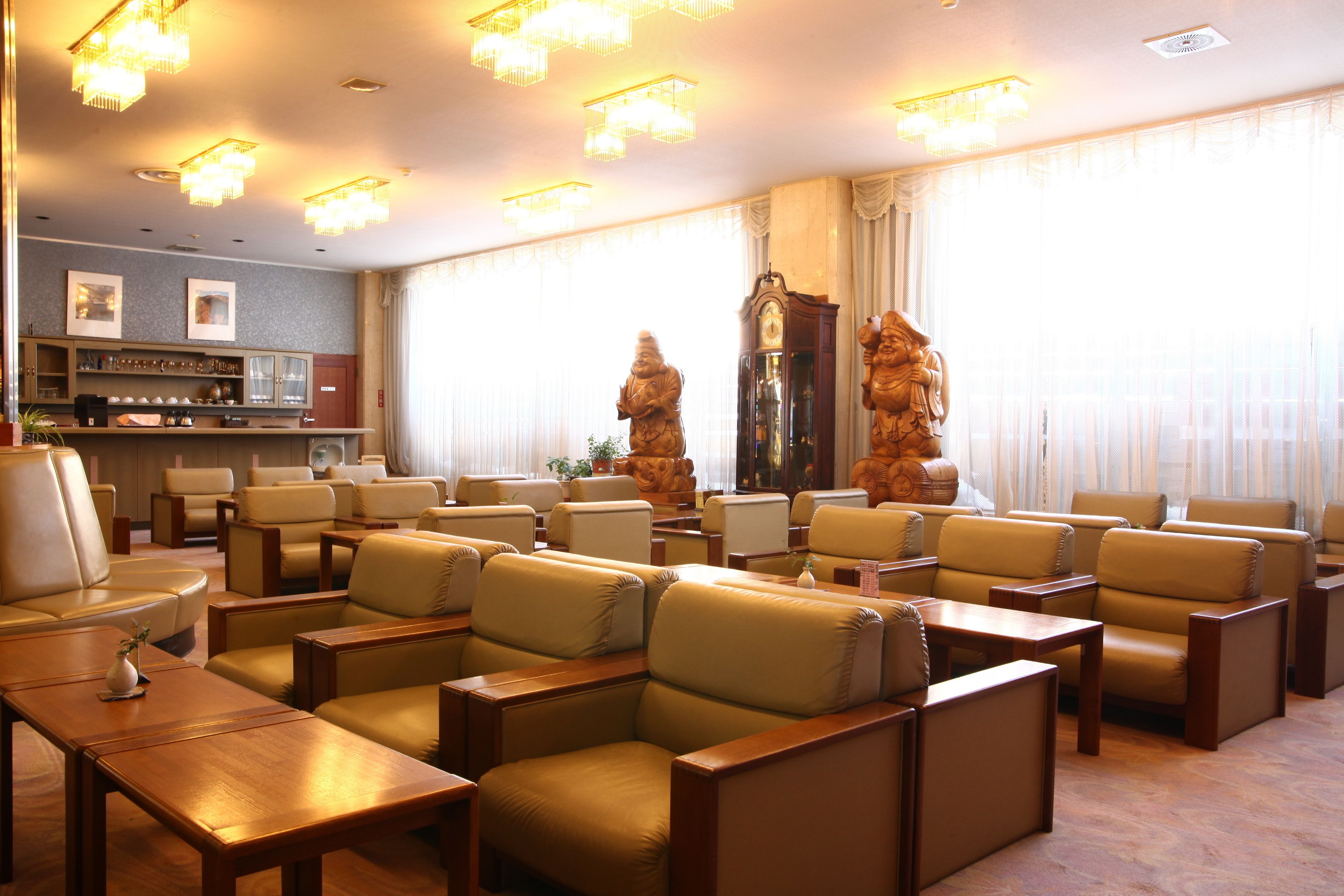Un hall de hotel con sofás de cuero, mesas de madera, una zona de bar y ventanas amplias con cortinas.