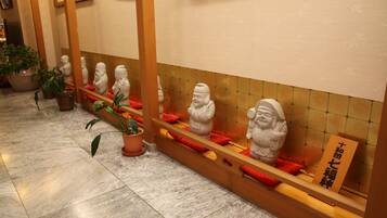 Un pasillo con una serie de estatuas de piedra en estanterías, plantas en macetas y un piso de baldosas.