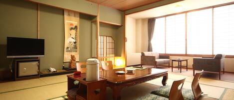 Une pièce de style japonais traditionnel, avec un sol recouvert de tatamis, une basse table en bois, des coussins, un téléviseur et des portes coulissantes.
