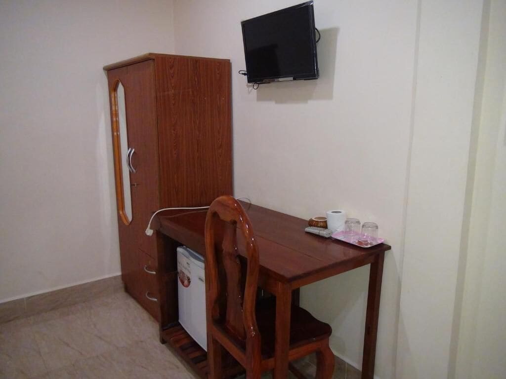 A compact room with a wooden desk, a television mounted on the wall, and a wardrobe.