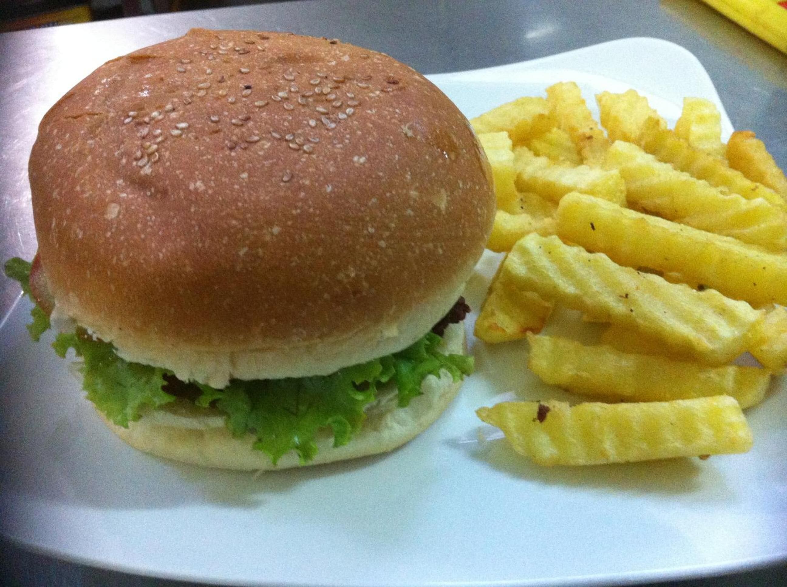 Hamburguesa con lechuga y una porción de papas fritas sobre un plato blanco.