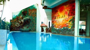 A swimming pool with a mural depicting a tropical scene with a volcano and a sunset. - Hotel Sanmark (Ahangama)