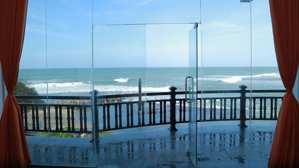 A balcony with a glass door overlooking the ocean. - Hotel Sanmark (Ahangama)