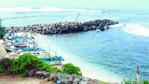 A beach with boats docked near a rocky breakwater. - Hotel Sanmark (Ahangama)
