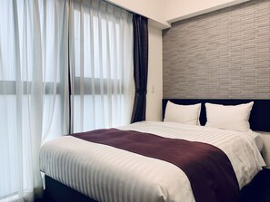 A modern hotel room with a large bed, a brick-patterned headboard, and sheer curtains. - Ueno Urban Hotel (Tokyo)