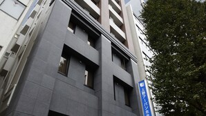 Um hotel moderno com uma entrada destacada e uma placa azul que indica ser o Ueno Urban Hotel.
