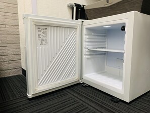 Un refrigerador blanco con pantalla digital, situado en una habitación con pared texturizada y piso alfombrado.