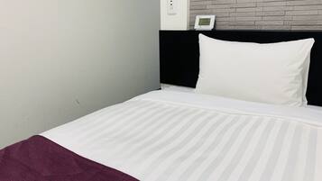 Una habitación de hotel con una cama, cabecera negra, almohada blanca, cubrecama a rayas blancas y una manta roja.