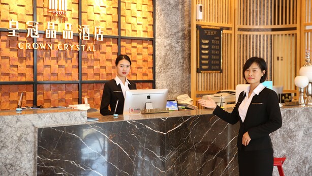 A hotel reception desk with a marble counter, a digital display, and a wooden wall with a grid pattern. - Crown Crystal Hotel (Shanghai)