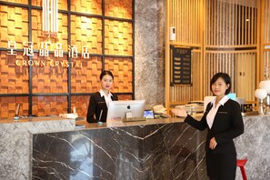Un comptoir d’accueil d’hôtel avec un plan de travail en marbre, un écran numérique et un mur en bois orné d’un motif quadrillé.