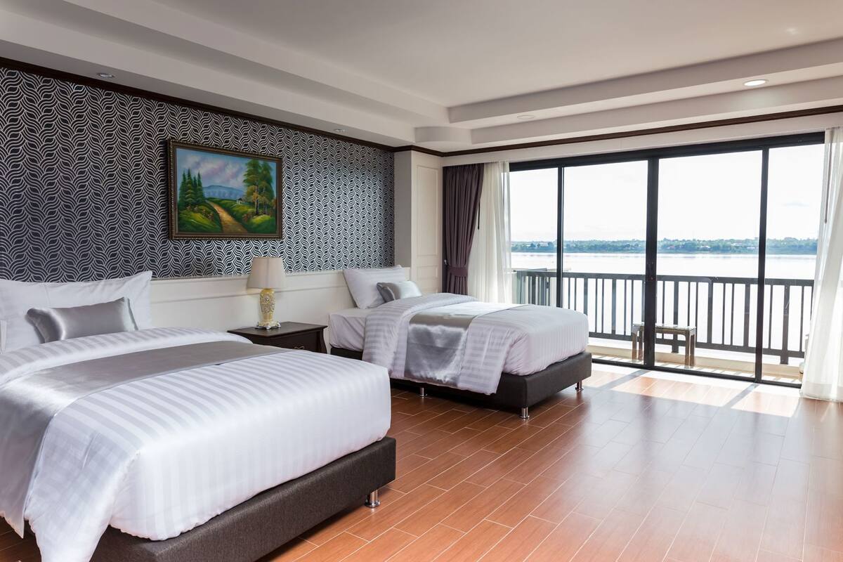 Ein Hotelzimmer mit zwei Betten, einem großen Fenster mit Blick auf das Wasser und einer Wand mit Muster.
