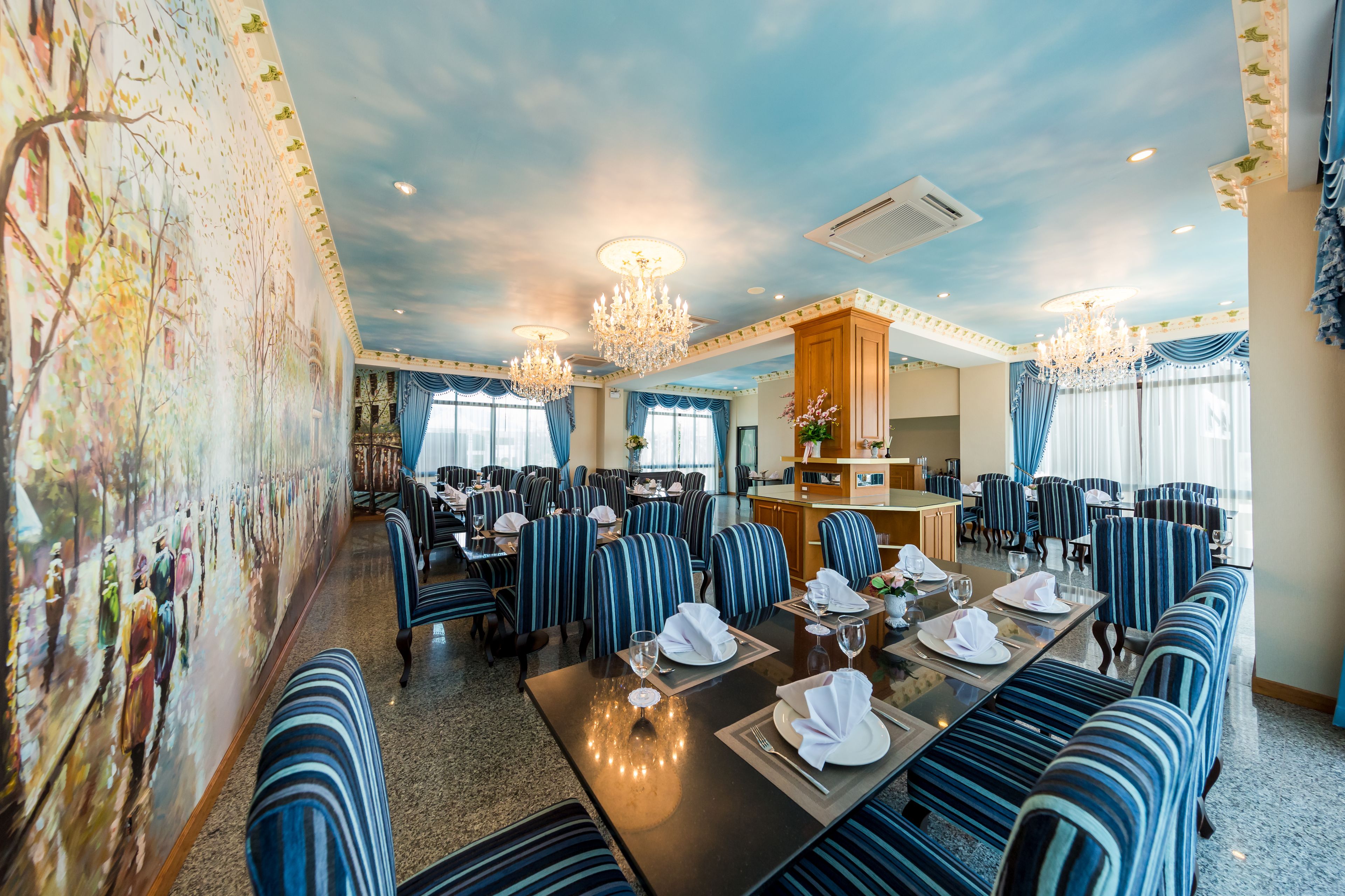 Een restaurantgedeelte in een hotel met gestreepte stoelen, gedekte tafels en een muurschildering.