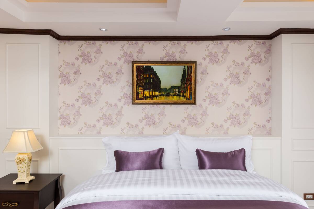 Ein Hotelzimmer mit Bett, Nachttisch, Lampe und einem gerahmten Bild an der Wand.