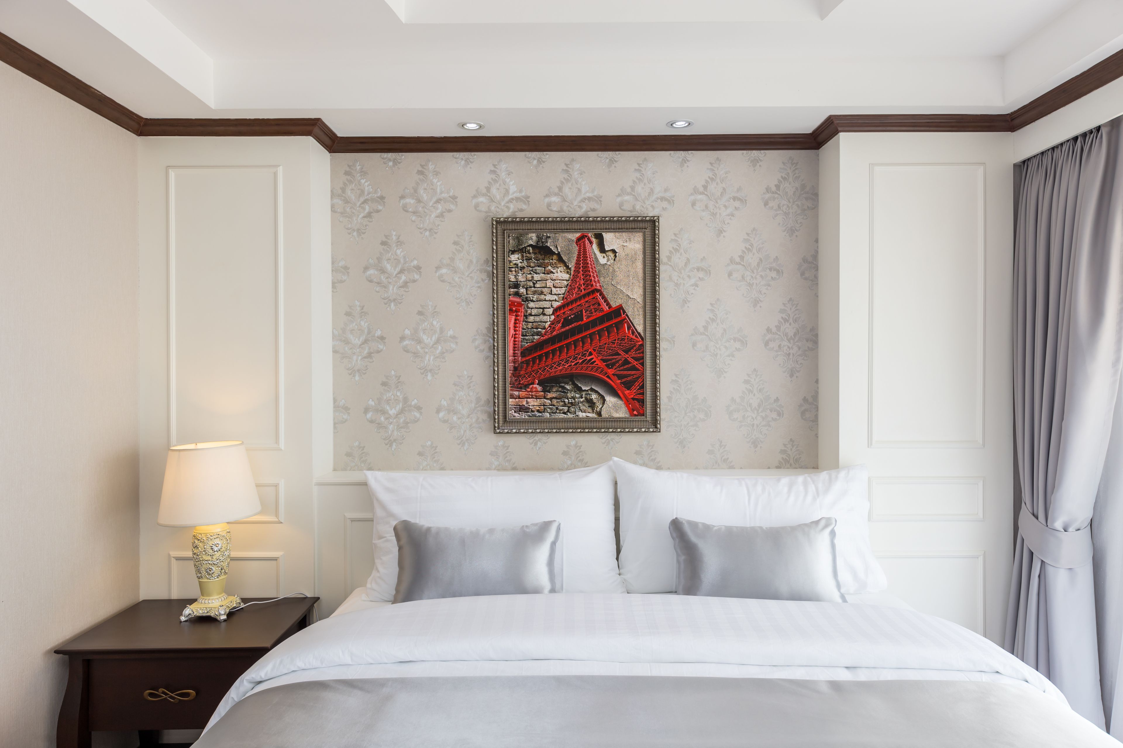 Una habitación de hotel con cama, una mesita de noche con lámpara y una pared decorada con un cuadro de la Torre Eiffel.