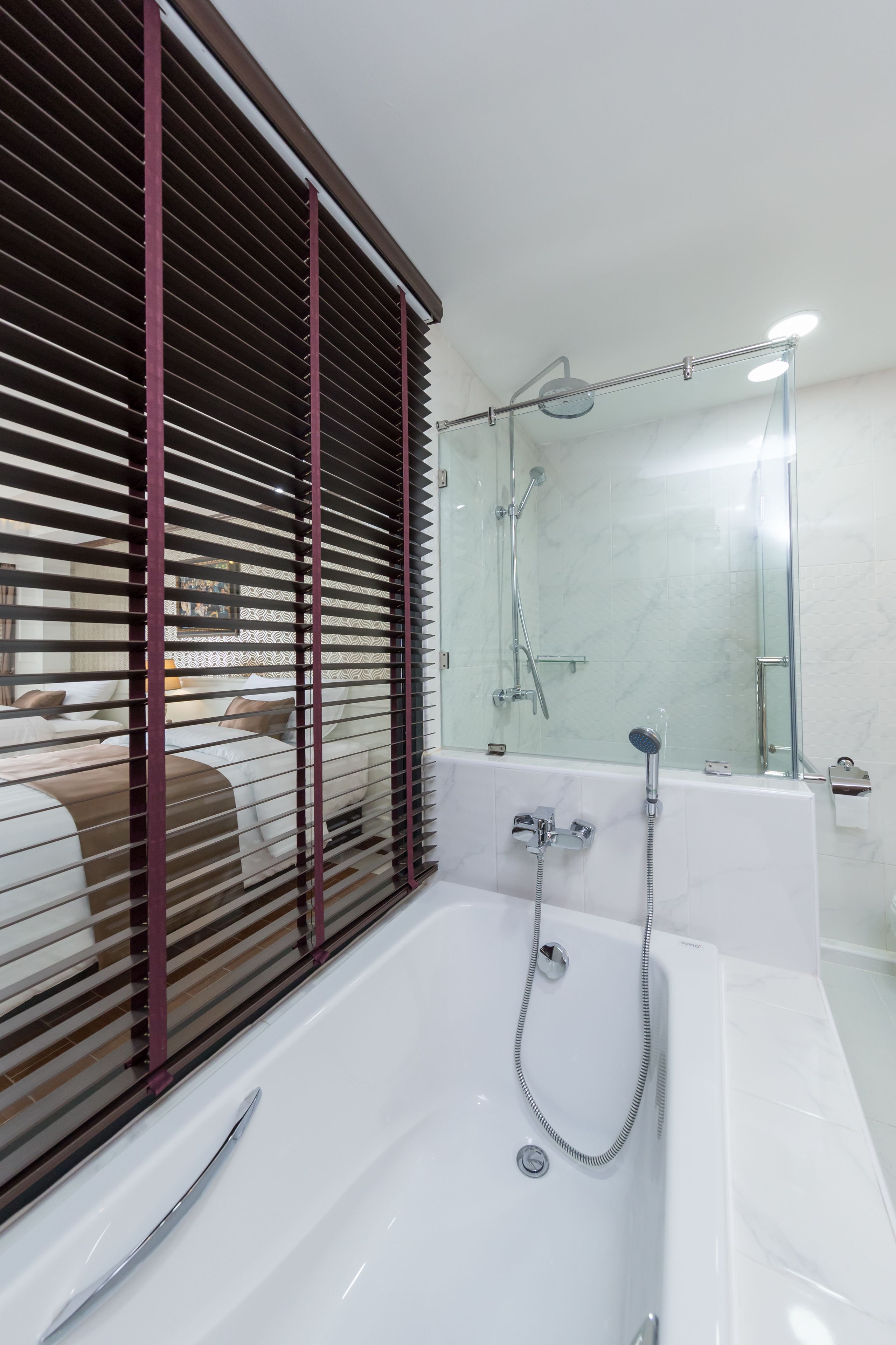 A modern bathroom with a large bathtub, a glass shower enclosure, and a window with blinds.